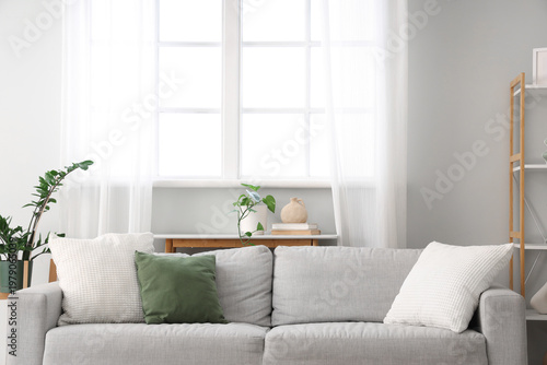 Interior of light living room with grey sofa and window