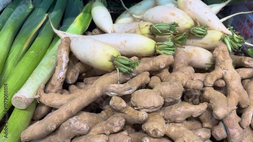 Fresh ginger and radishes at a local market in the afternoon with green onions in the background