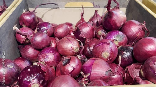 Fresh red onions gathered in a wooden box at a market during the day