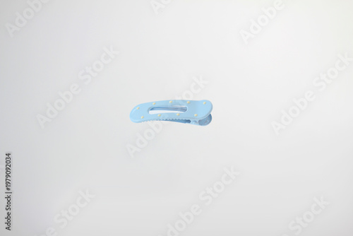 Light soft blue hair clip rests on plain white surface. Minimalist design catches eye with clean lines, with decorative dot details,  simple curved design and secure clasp isolated on white background