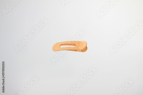 Light soft orange hair clip rests on plain white surface. Minimalist design catches eye with clean lines, with decorative dot details, simple curved design, secure clasp isolated on white background