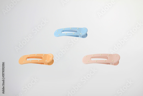 Pastel colored hair clips float against a clean white background. Minimalist plastic hair accessories in soft blue, peach, and pink colors with decorative dot details arranged in balanced composition 