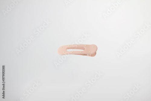 Light soft pink hair clip rests on plain white surface. Minimalist design catches eye with clean lines, with decorative dot details, simple curved design and secure clasp isolated on white background