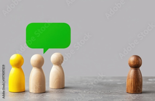 Four wooden figures with one yellow, two natural, and one brown, with a green speech bubble above the trio, symbolizing communication or social exclusion.