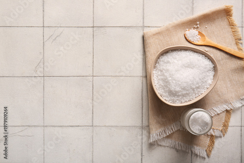 Composition with bowl of sea salt, spoon and napkin on light tile background