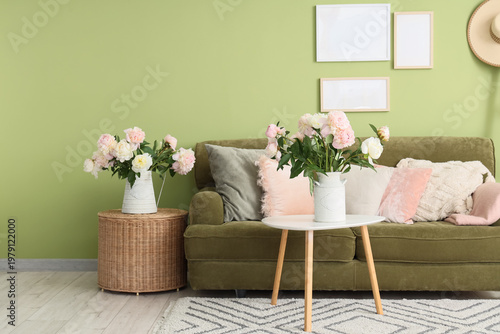 Interior of stylish living room with green sofa, coffee table and beautiful peonies