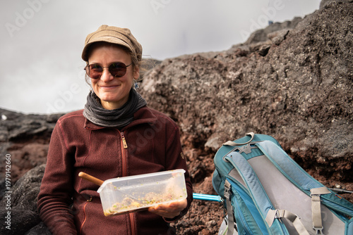 Schilderij op canvas Mujer joven con gafas y sombrero comiendo en la montaña después de un día de senderismo