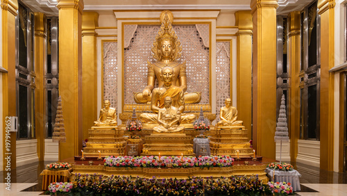 Fotografie A golden Buddha shrine fills the hall with seated statues and flower rows