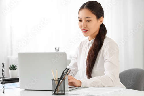 Young Asian businesswoman with modern laptop working at her workspace in office