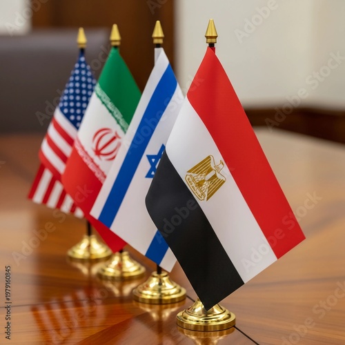 Flags of the United States, Iran, Israel, and Egypt stand together on a polished wooden table in a room with a blurred background.