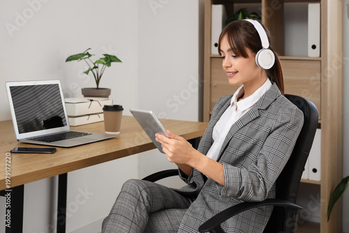 Beautiful young businesswoman in headphones with modern tablet computer in of...