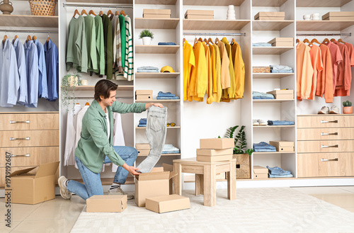 Foto Handsome young man unpacking wardrobe boxes with stylish clothes in dressing roo