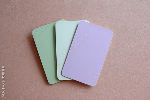 Three blank fanned out cards in mint and lavender pastel colors placed on a textured blush pink surface for stationery.