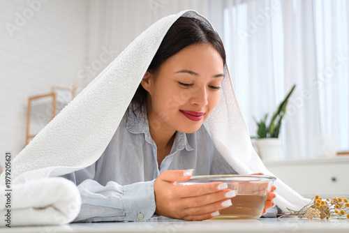Cuadro en lienzo Young Asian woman with towel doing steam inhalation at table in bedroom
