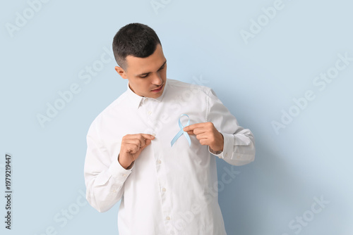 Handsome man with blue ribbon on color background. Prostate cancer concept