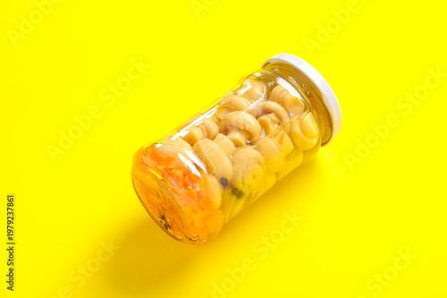 Jar with canned mushrooms on yellow background