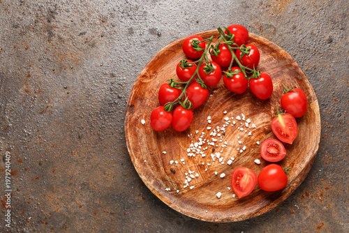 Wooden plate with fresh cherry tomatoes on dark background