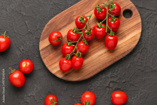 Wooden board with fresh cherry tomatoes on black background
