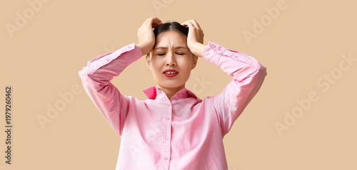 Young Asian woman suffering from headache on beige background