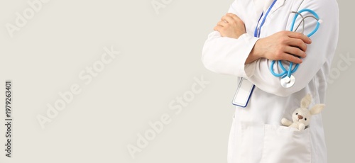 Male pediatrician with stethoscope and toy in his pocket on light background ...