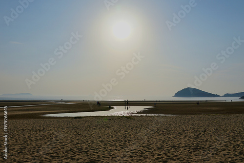 Φωτογραφία Silhouetted People Walking on Beach at Sunset With Distant Island and Calm Sea