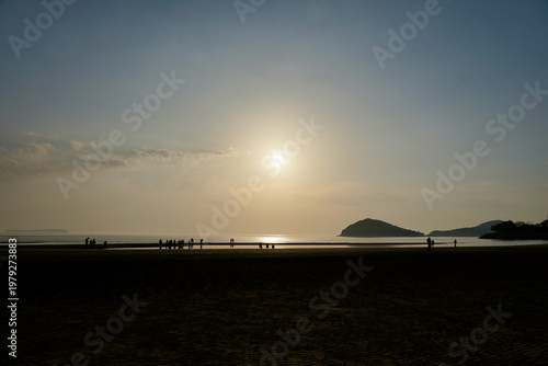 Canvastavla Silhouetted People Walking on Beach at Sunset With Distant Island and Calm Sea
