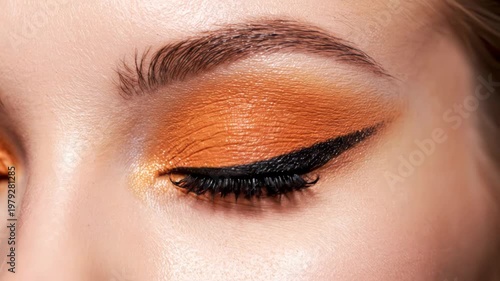 Closeup of a womans eye with vibrant orange eyeshadow and black eyeliner