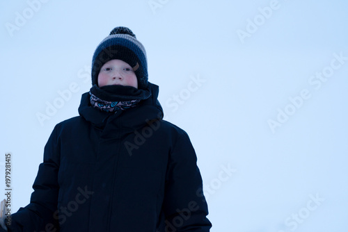 A teenager in winter clothes against a snowy winter backdrop of the sea. A boy with rosy cheeks on a nature walk. Concept of recreation, sports, and people. High quality photo