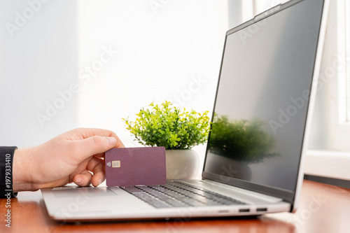 Person holding a credit card while using a laptop for online shopping and financial transactions, close-up 