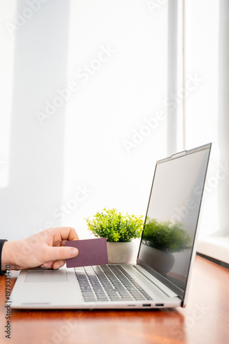 Person holding a credit card while using a laptop for online shopping and financial transactions, close-up 
