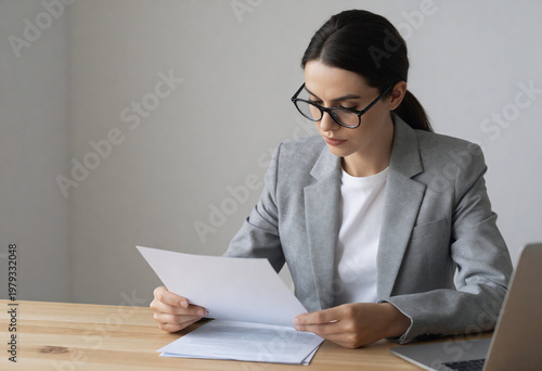 Professional Businesswoman Reviewing Documents at Office Desk with Laptop, Focused Corporate Work Environment.