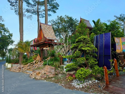 A traditional Thai-style garden with ornate wooden structures, lush greenery and bamboo stairs