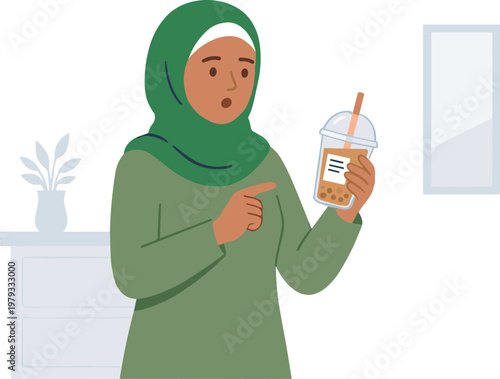 A surprised woman wearing a green hijab holds and points at an iced coffee drink in a modern indoor setting.