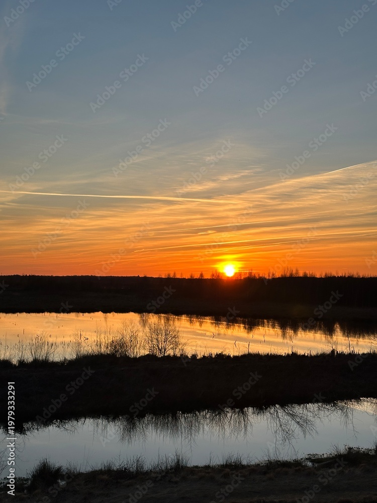 Obraz premium A stunning sunset where the sky is ablaze over the Himmelmoor. A lake can be seen in the background.