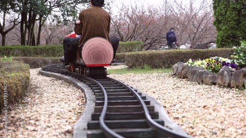 Child enjoying a ride on a small steam locomotive at a public park, focus on the moving train and wheels.