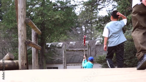 Slow motion of a boy playing on a zip line or rope swing at an outdoor adventure park, rear view.