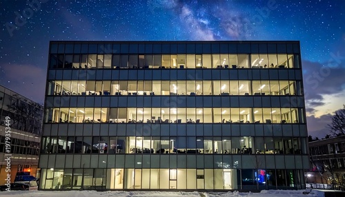 Modern office building at night, illuminated by interior lights, contrasting with a starry night sky. The building?s facade is visible