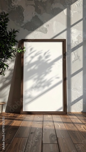 Vertical shot of a wooden framed blank picture propped against a textured gray wall, lit by sunlight creating shadow play
