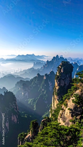 A breathtaking panoramic view showcases the majestic Huangshan mountains shrouded in mist, with verdant peaks rising dramatically against a clear blue sky.
