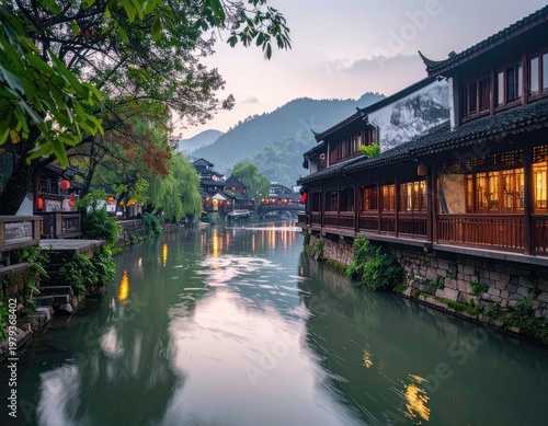 A serene view of a traditional Chinese water town showcases ancient architecture reflected in the tranquil canal, framed by lush greenery and distant mountains.