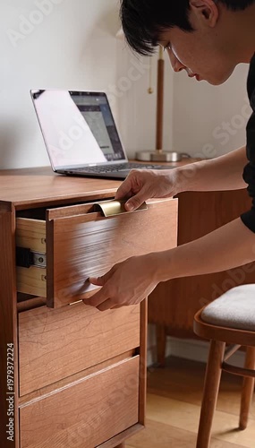 Person working at desk opening drawer near laptop
