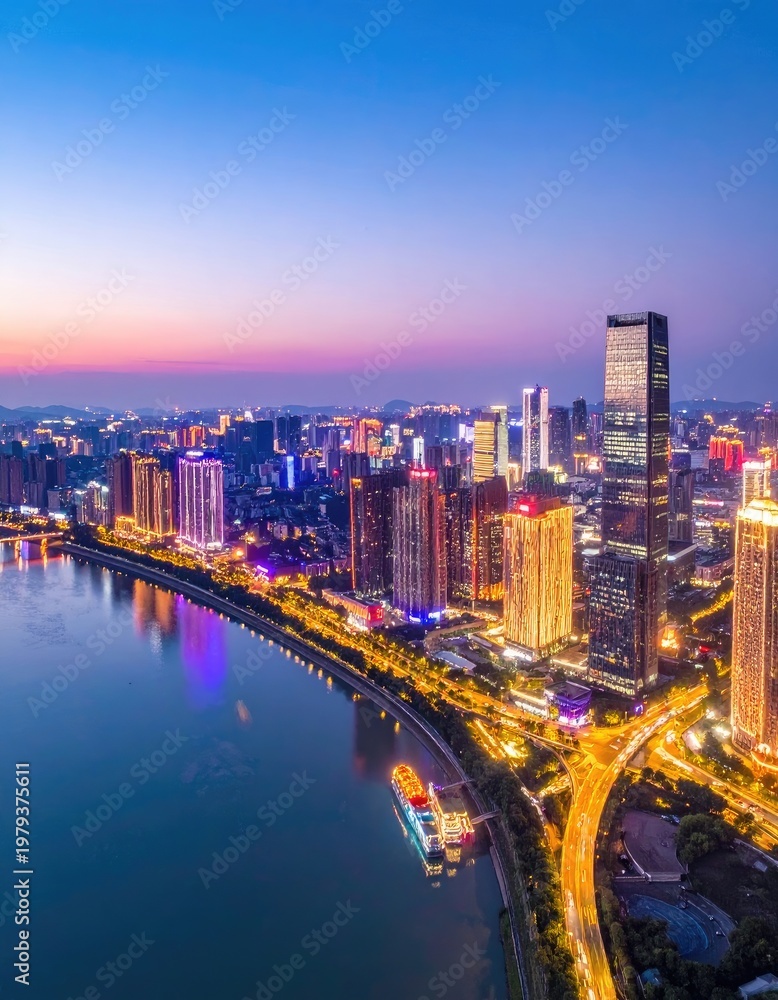 Obraz premium An aerial view showcases a vibrant cityscape illuminated at dusk, with a river winding through the urban landscape and a stunning sunset painting the sky with warm hues.