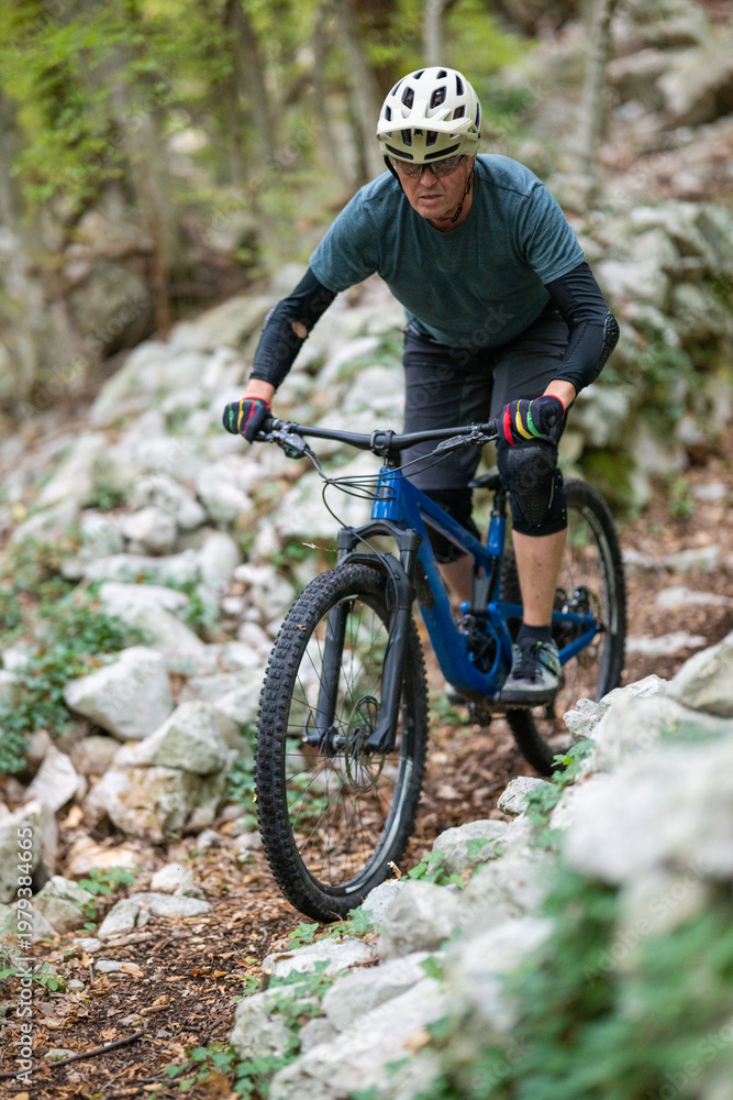Fototapeta premium Experienced cyclist mountain biking on a rocky forest trail wearing helmet and protective gear