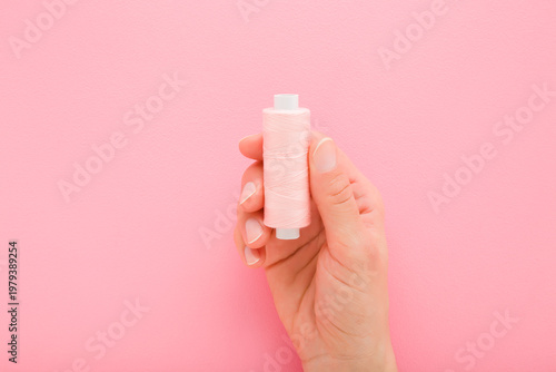 Bild auf Leinwand Young adult woman hand holding and showing new pink thread spool on light pink table background