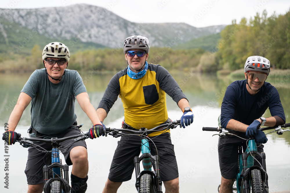 Obraz premium Three friends mountain biking by a lake enjoying outdoor adventure and fitness together