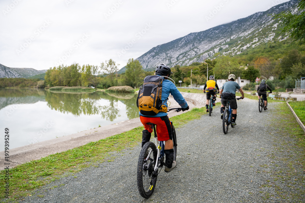 Obraz premium Group mountain biking along a lakeside trail with cyclists enjoying outdoor adventure