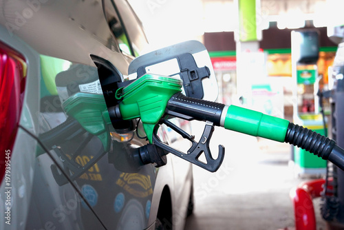 Obraz na plátne Fuel nozzle inserted into car tank at gas station, green handle close-up