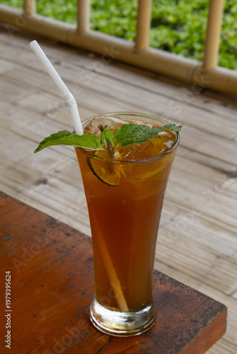 Glass of fresh iced lemon tea with mint leaves on wooden table