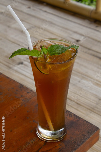Glass of fresh iced lemon tea with mint leaves on wooden table