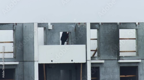 Construction worker on ladder inside unfinished multi-story residential building. Structure of grey prefabricated concrete wall slabs. Building development project, exposed framework.